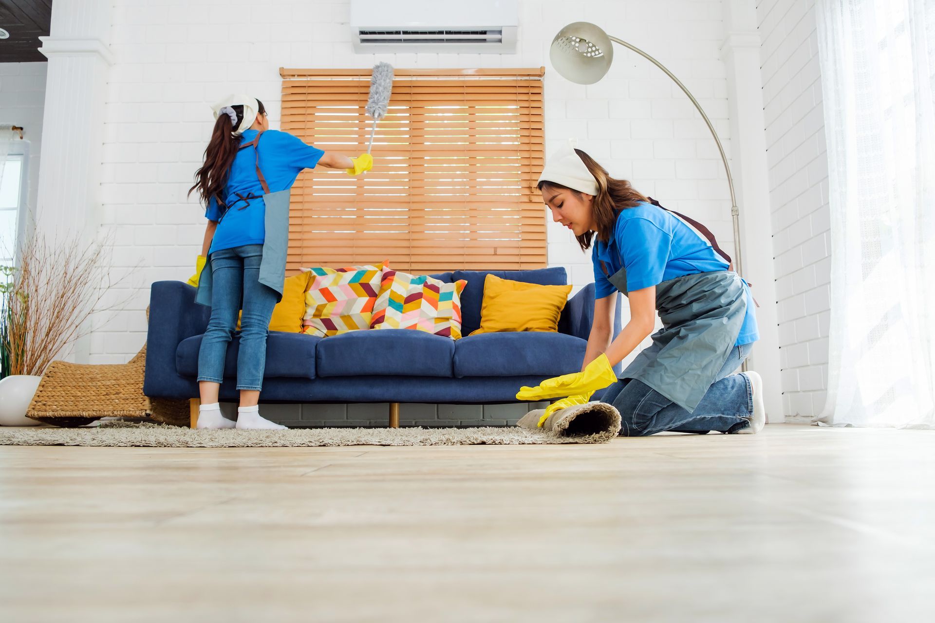 Two people cleaning a bright living room with yellow gloves and dusting tools Two people cleaning a bright living room with yellow gloves and dusting tools