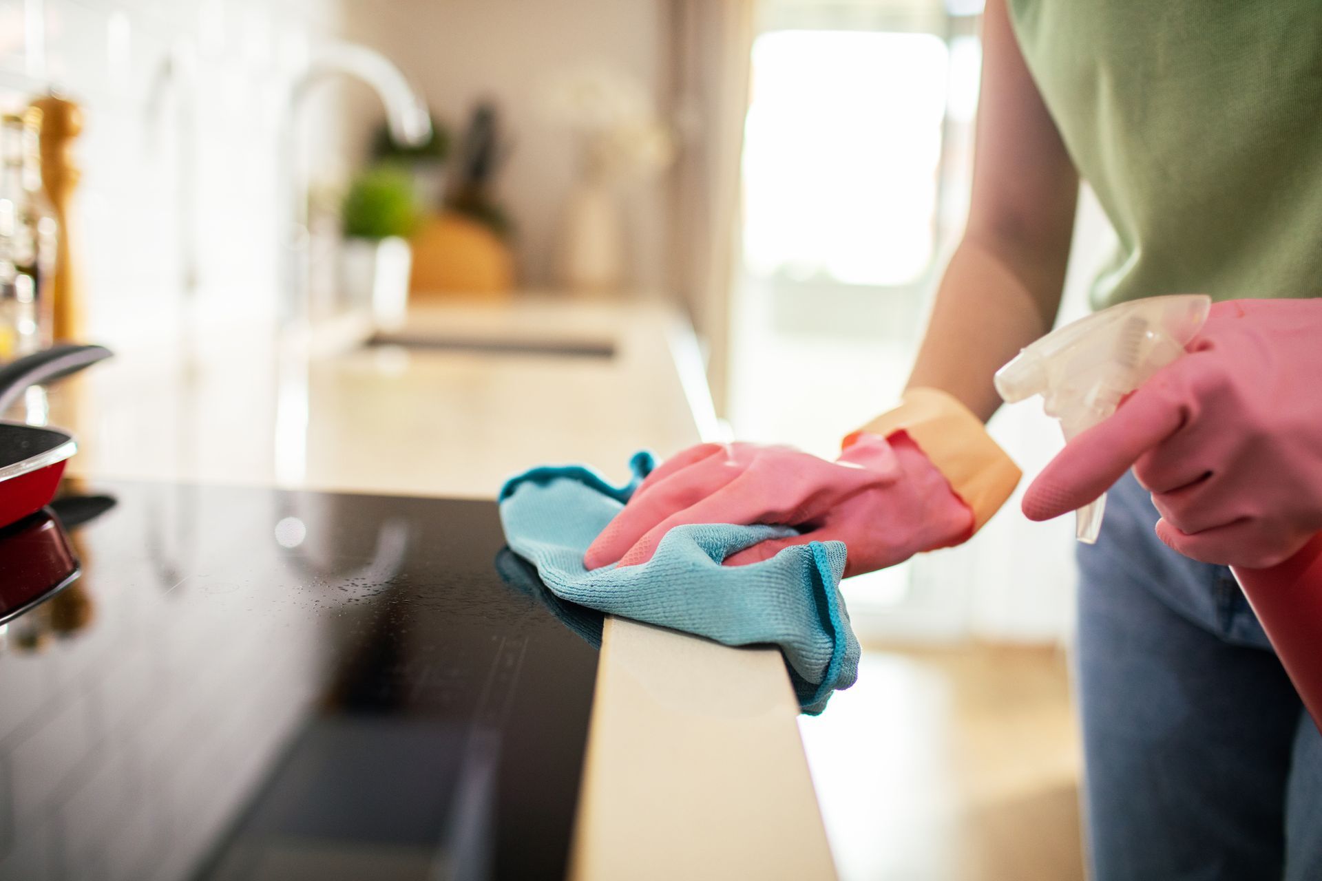 Person wearing pink gloves wiping a countertop with a blue cloth in a kitchen Person wearing pink gloves wiping a countertop with a blue cloth in a kitchen