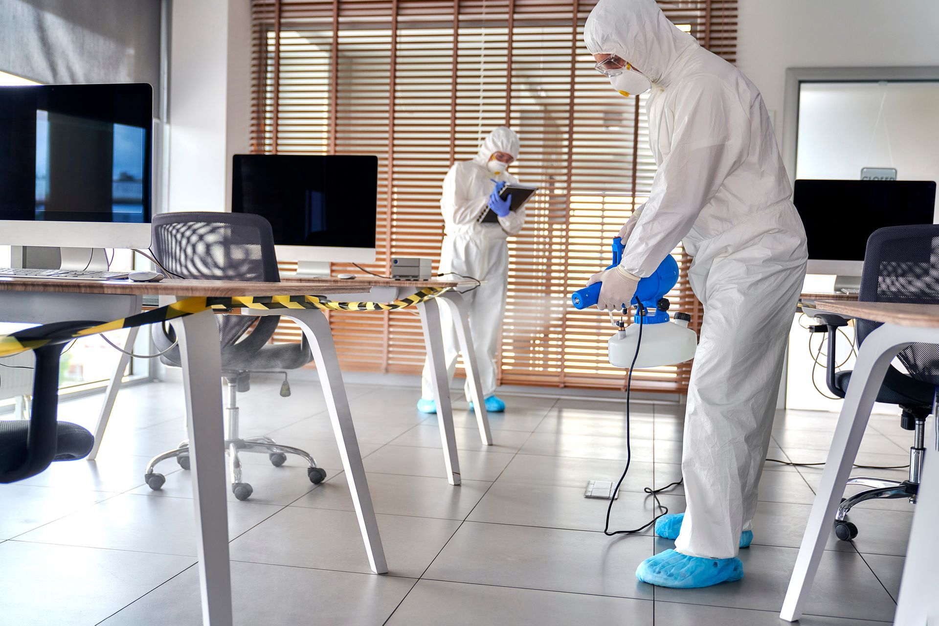 People in white hazmat suits and blue gloves disinfecting an office with spraying equipment