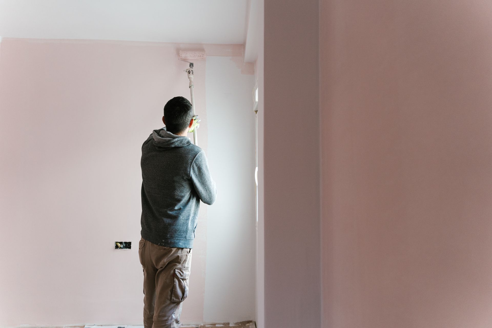 Person standing in a bare room, looking out a window with pink walls and a doorway visible. Person standing in a bare room, looking out a window with pink walls and a doorway visible.
