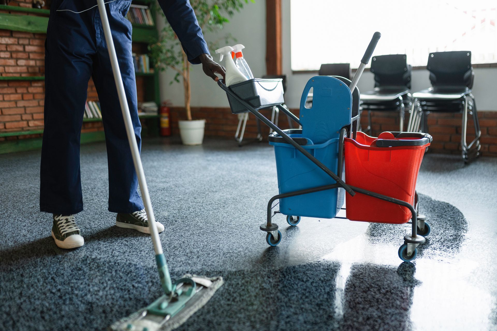 Person mopping a wet patio beside a blue and red cleaning cart with supplies.