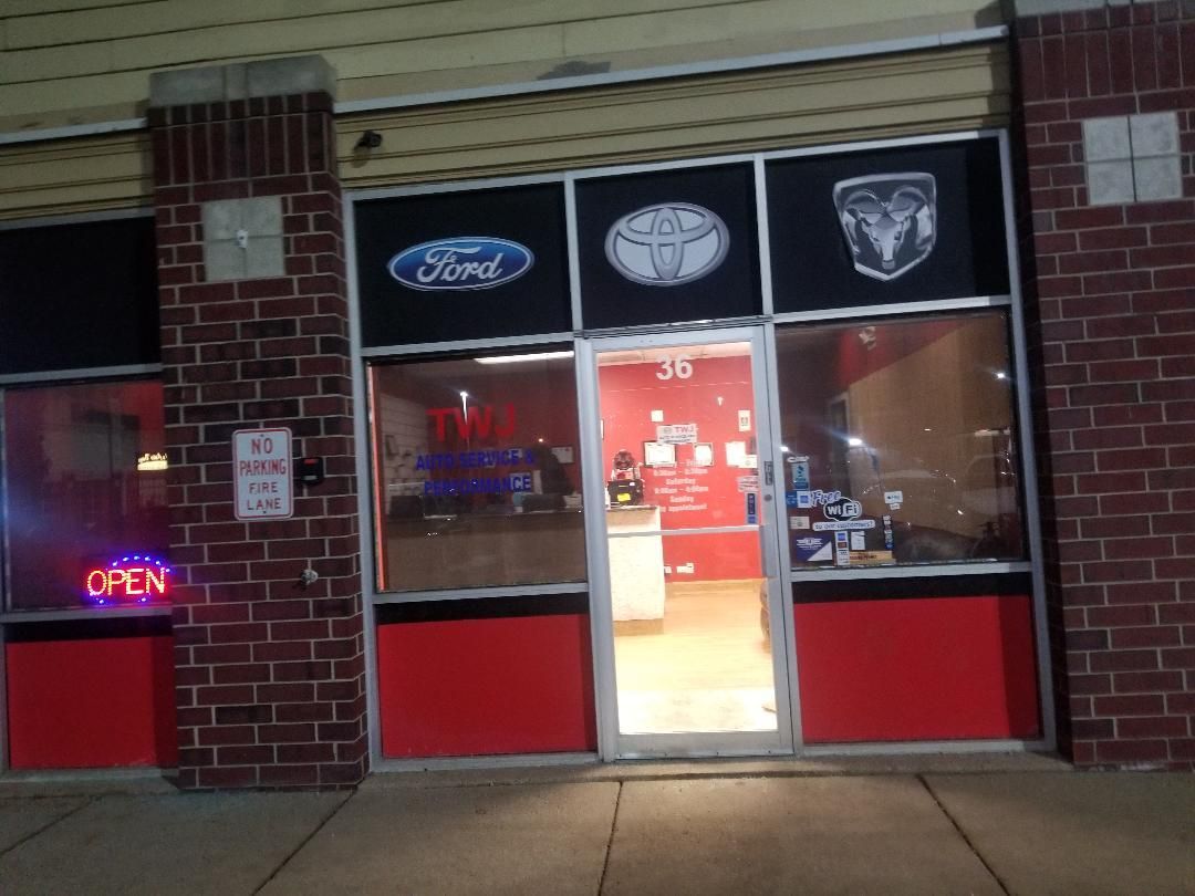 Storefront with illuminated open sign, glass door, and car brand logos above the entrance at night.