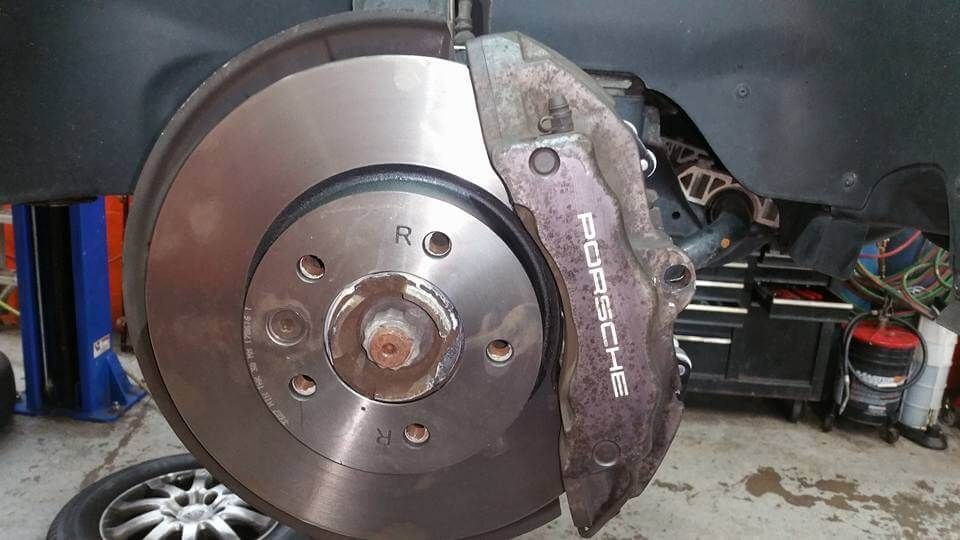 Car brake rotor and caliper with wheel removed, shown inside a garage.