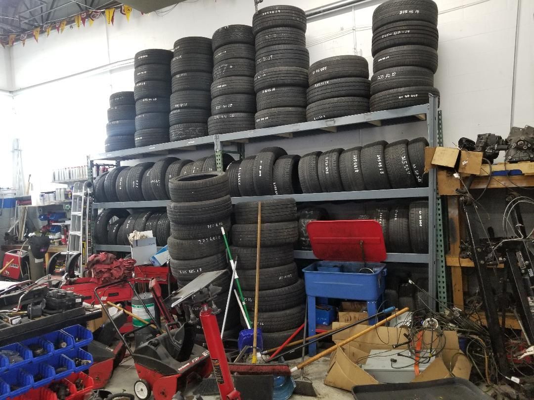 Garage storage shelves stacked with tires, car parts, and assorted tools in a cluttered workshop