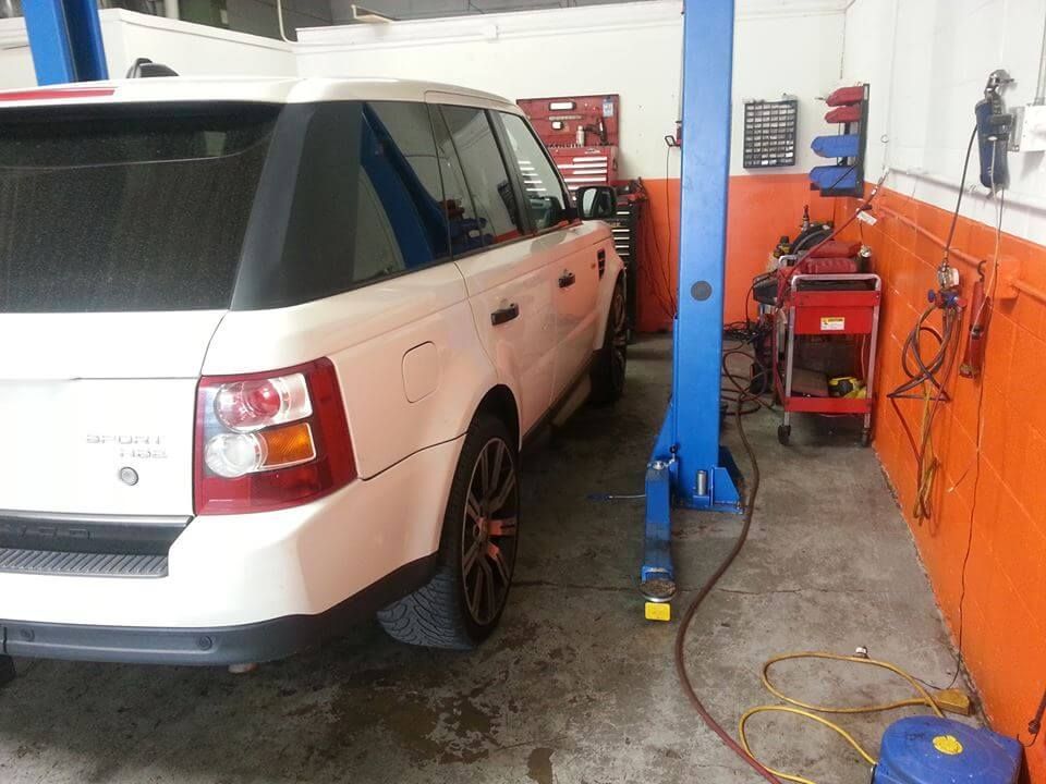 White SUV in an auto repair bay next to a blue lift and orange walls