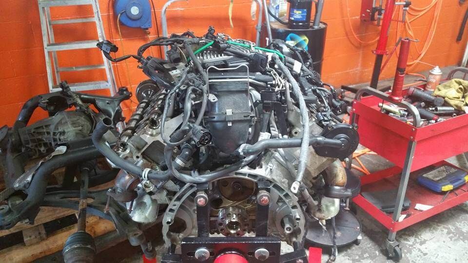 Car engine on a stand in a garage, surrounded by tools and orange walls