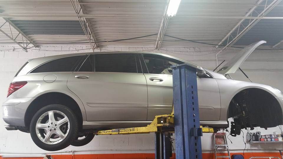 Silver SUV on a car lift in an auto repair shop, with the front wheel removed.