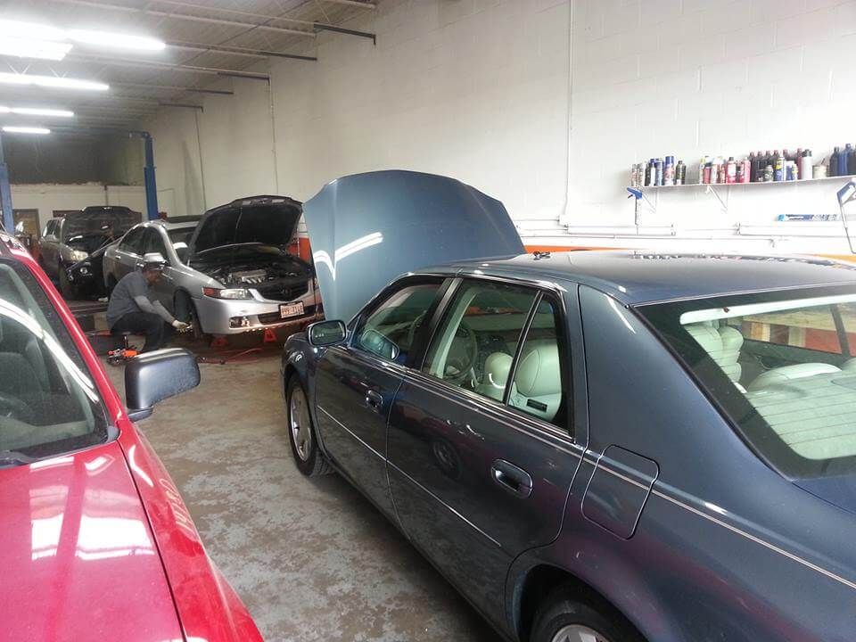 Auto repair shop with several parked cars, including a dark sedan with its hood open.