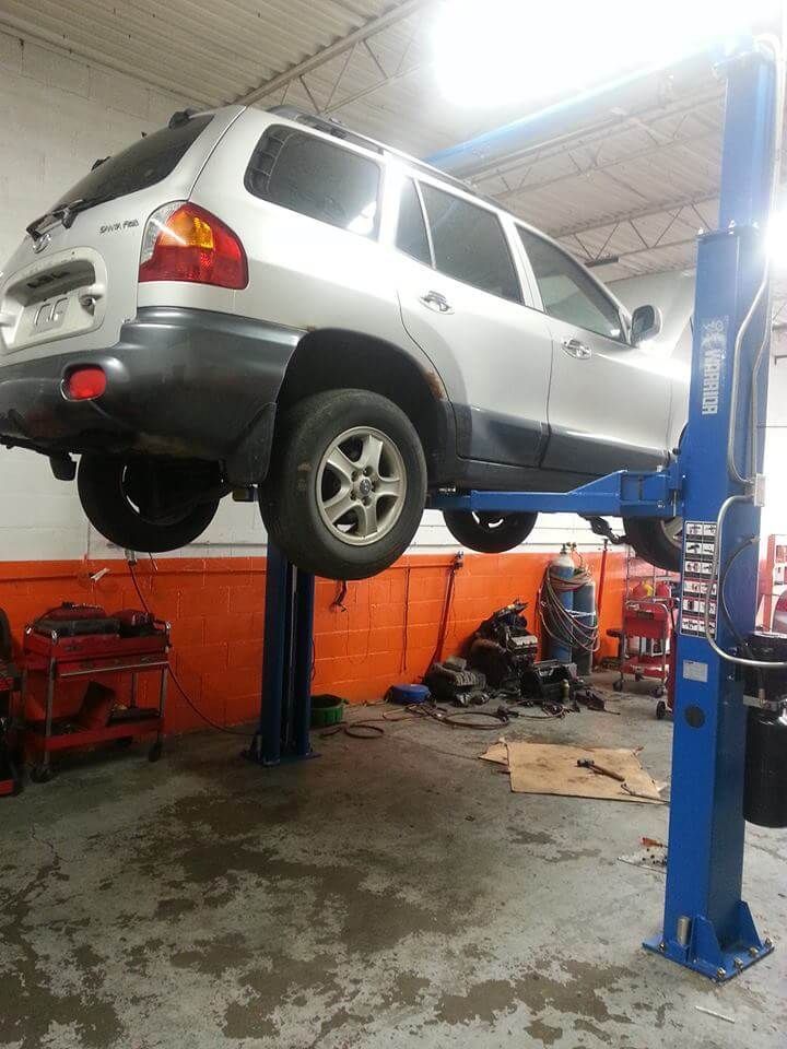 Silver SUV raised on a blue hydraulic lift in an auto repair shop, with tools and equipment below.