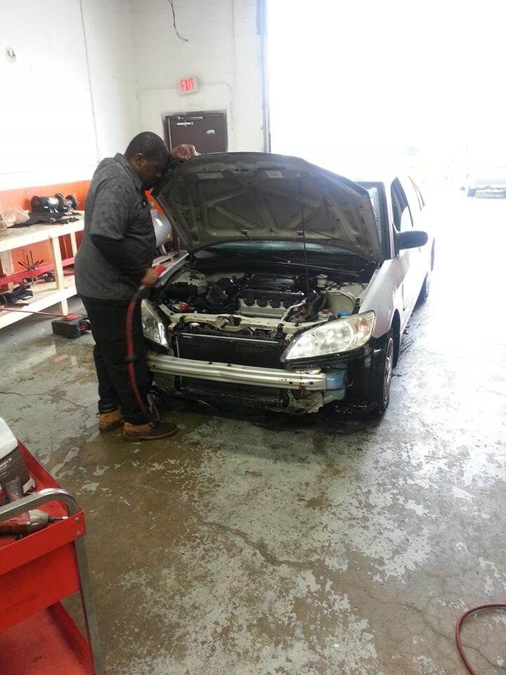 Mechanic inspecting a damaged black car with its hood open in a repair garage