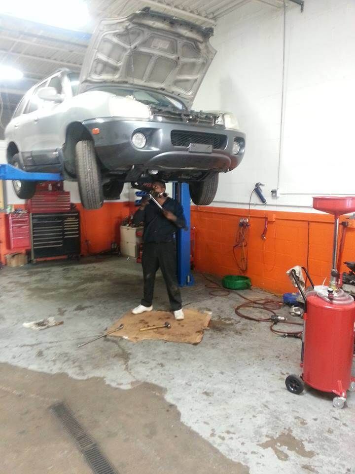 Mechanic working under a raised silver car in an auto repair garage