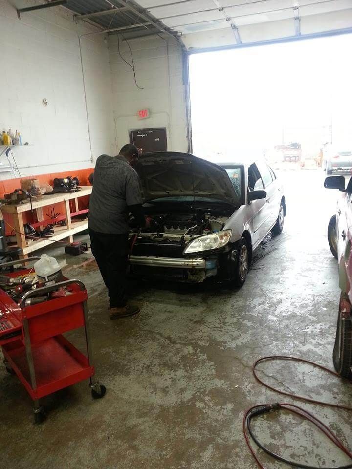Mechanic working on a black car with open hood in an auto repair garage