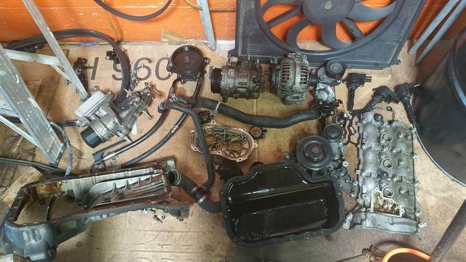 Assorted car engine parts and tools scattered on a cardboard-covered floor in a workshop.