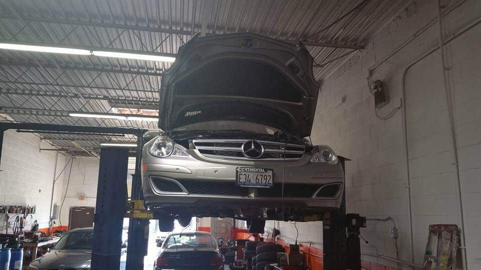 Car lifted on a hoist in a garage with its hood open, front end raised for repair.