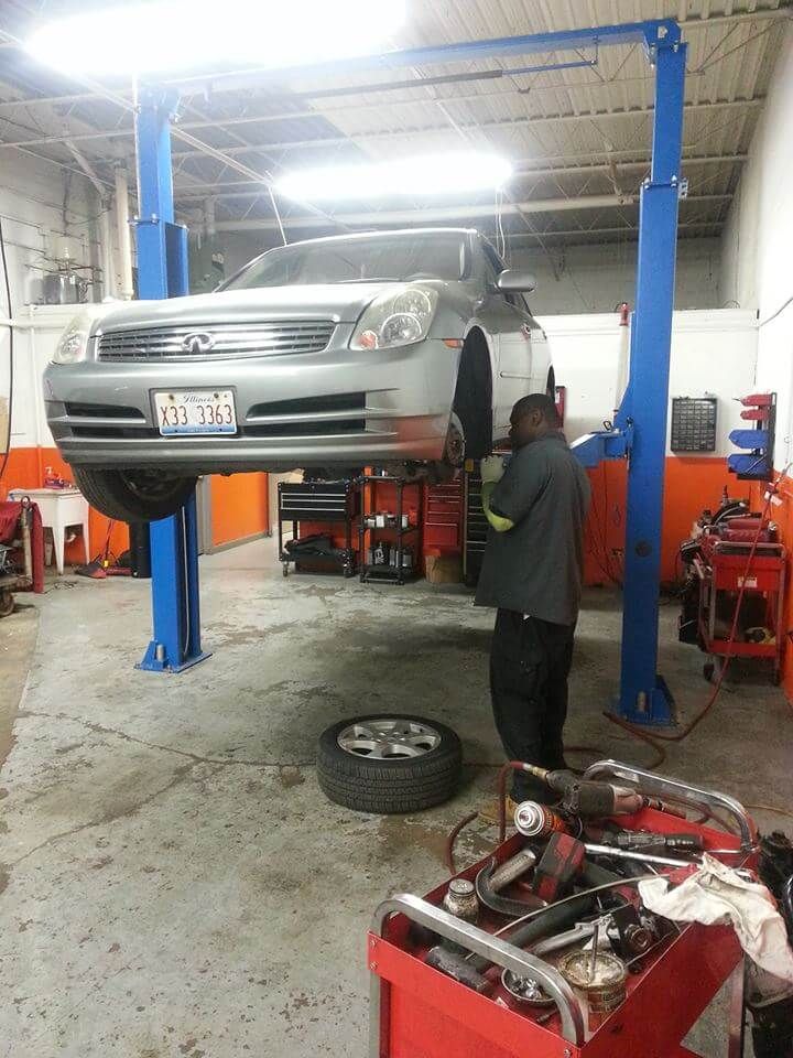 Silver car lifted on a blue auto hoist in a repair shop, with a mechanic working underneath.