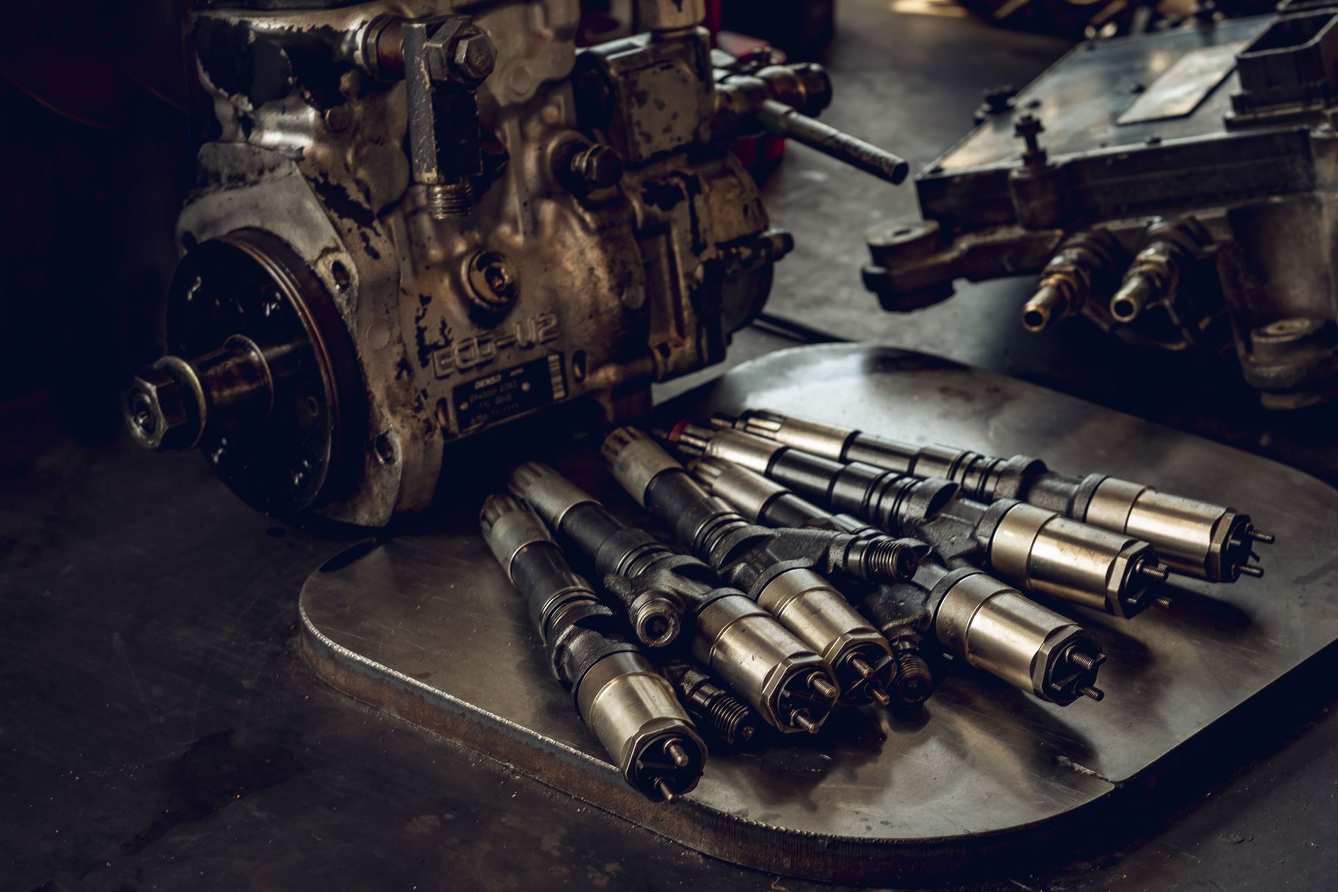 Metal machine parts and precision tools laid out on a workshop table beside a disassembled engine block.