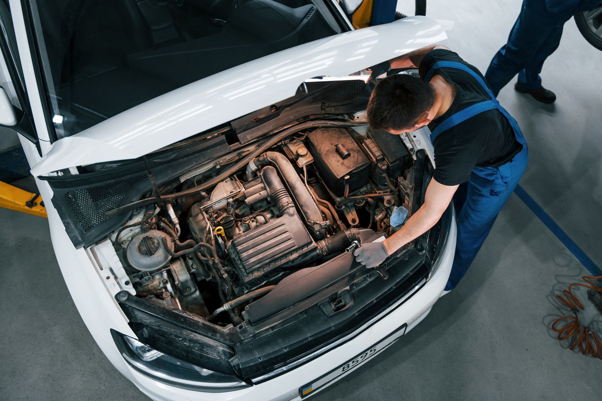 Mechanic inspecting a car engine under an open hood in a workshop
