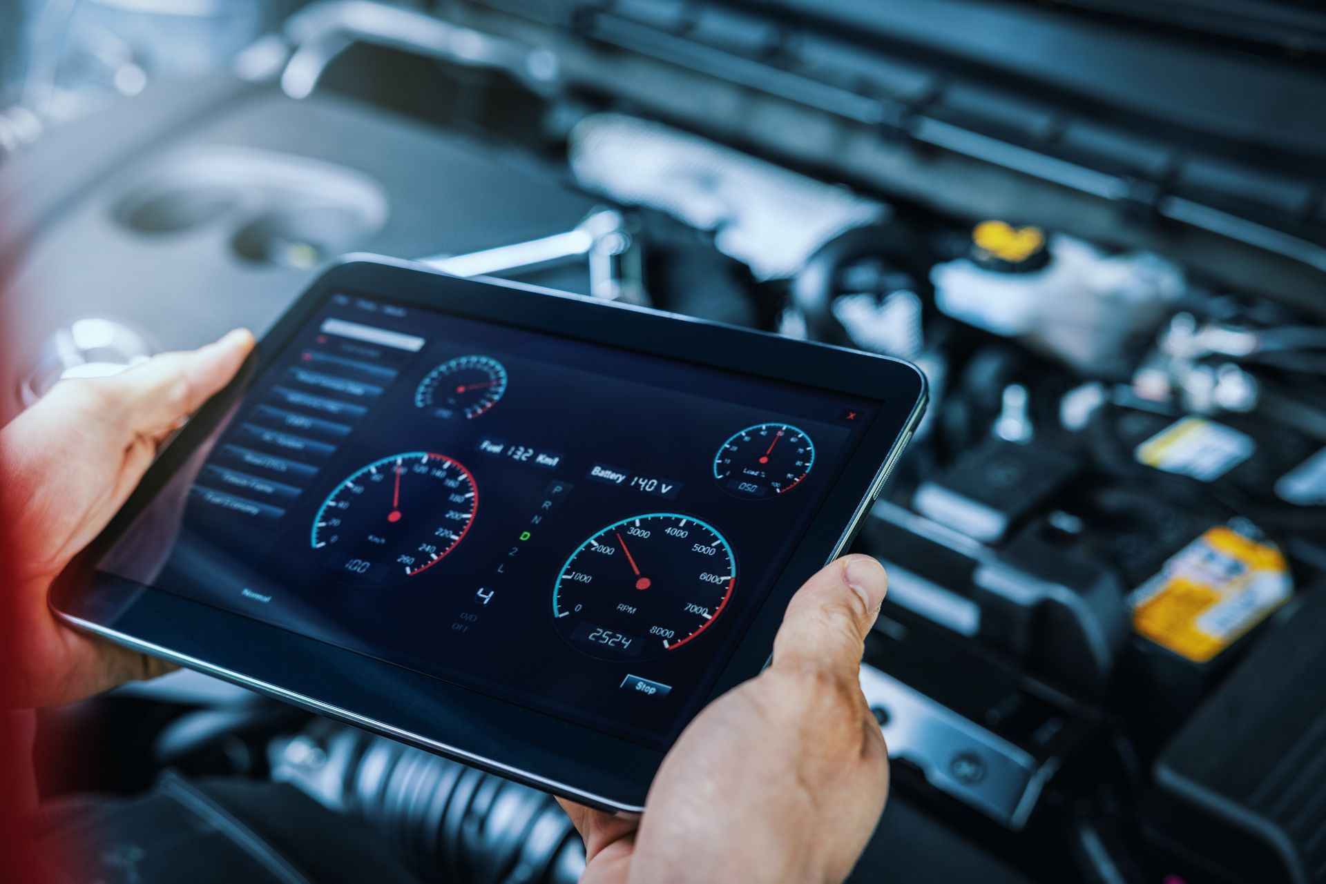 Hands holding a tablet displaying car diagnostics beside an open engine bay
