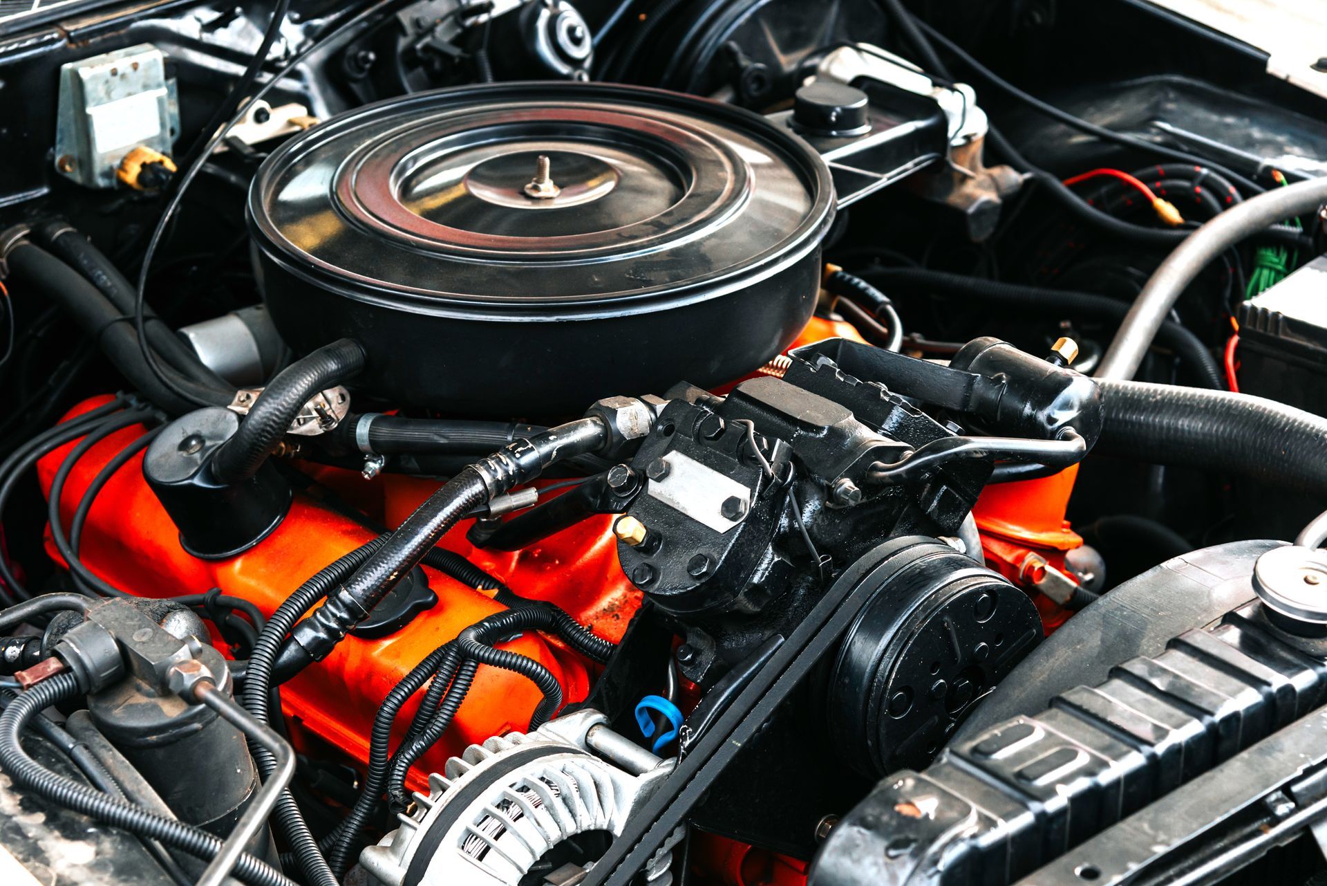 Close-up of a classic car engine with orange valve covers and a round air filter