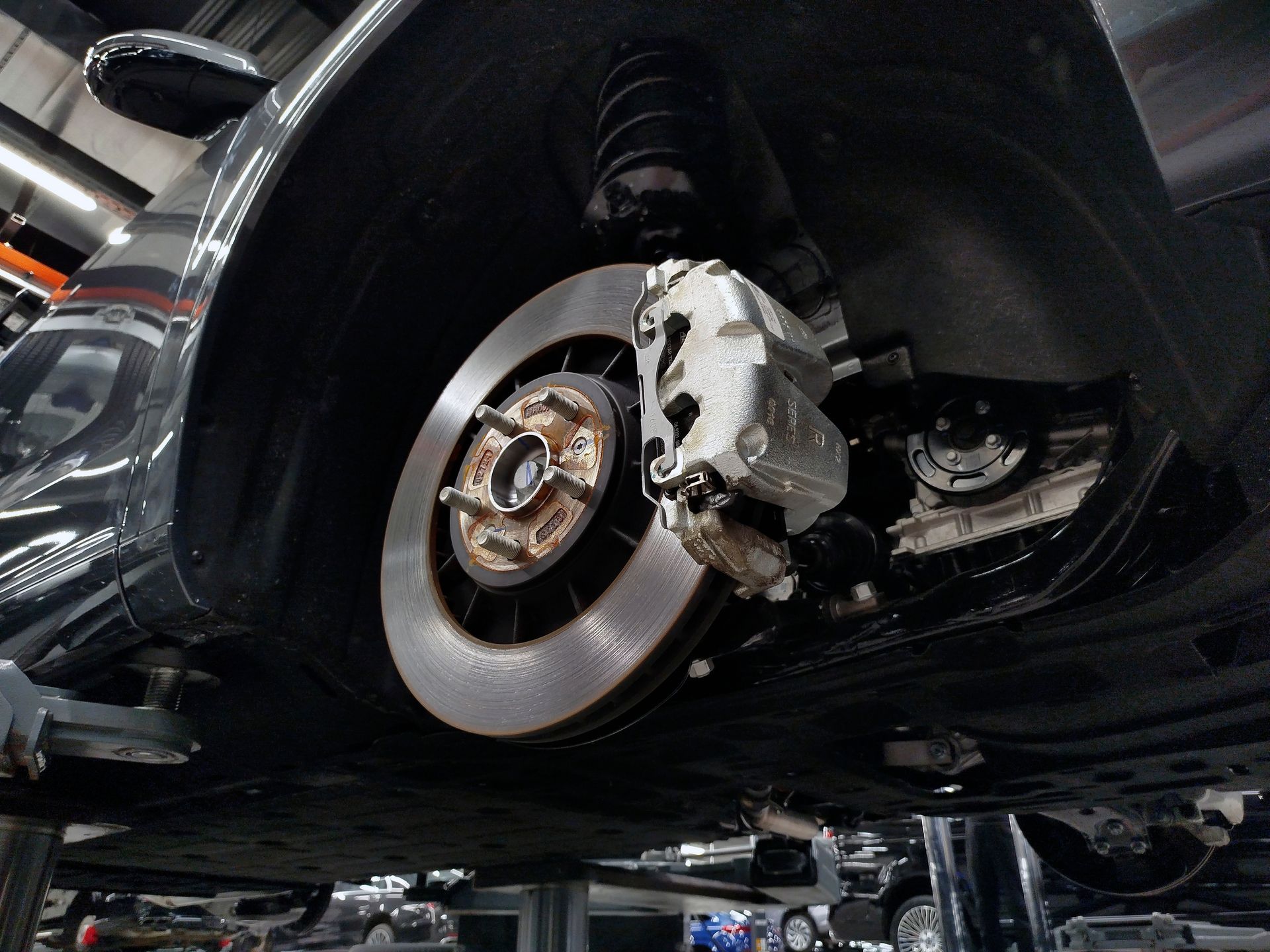 Car wheel removed in a garage, showing the brake rotor, caliper, and suspension.