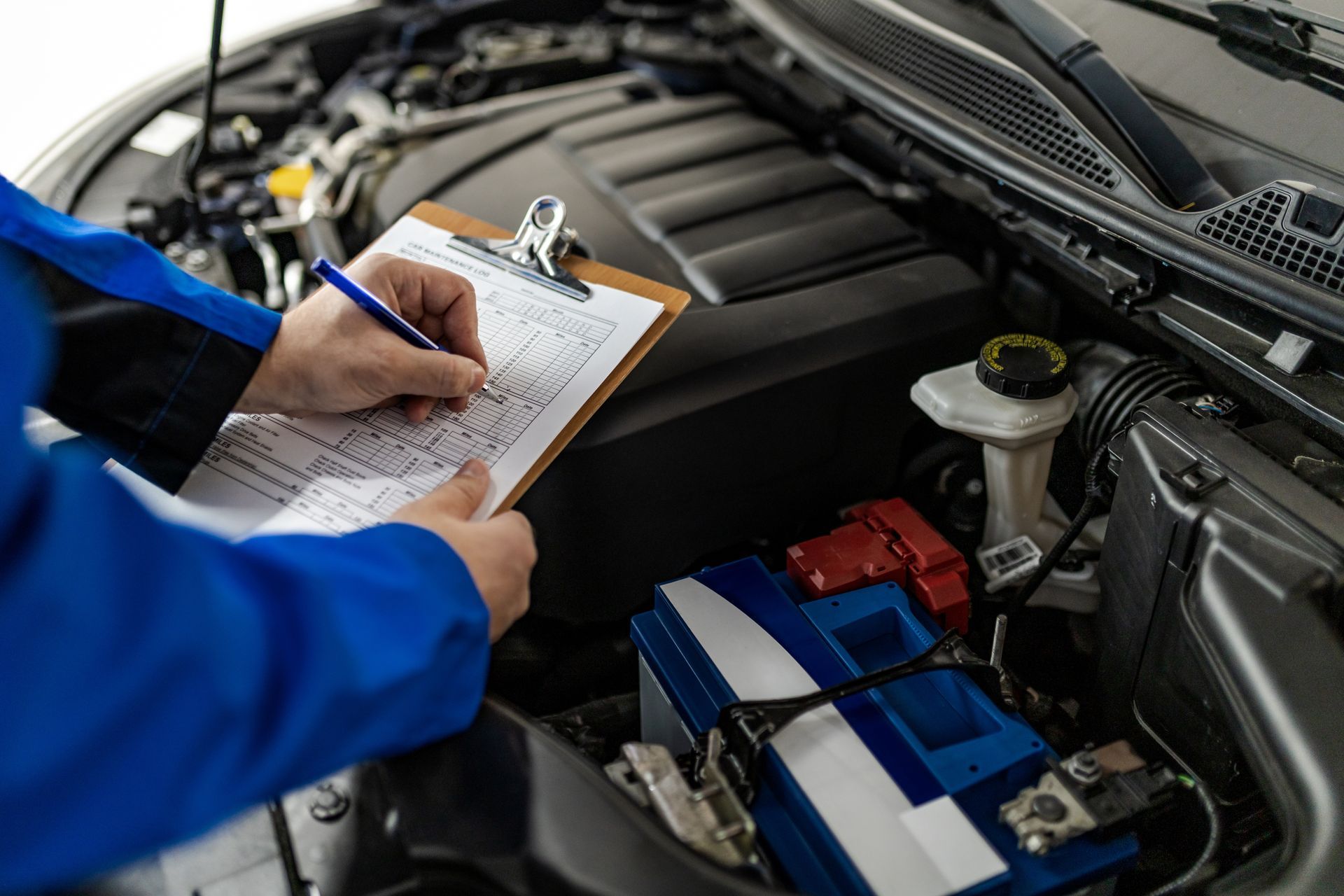 Mechanic writing on a checklist in a car engine bay with the hood open