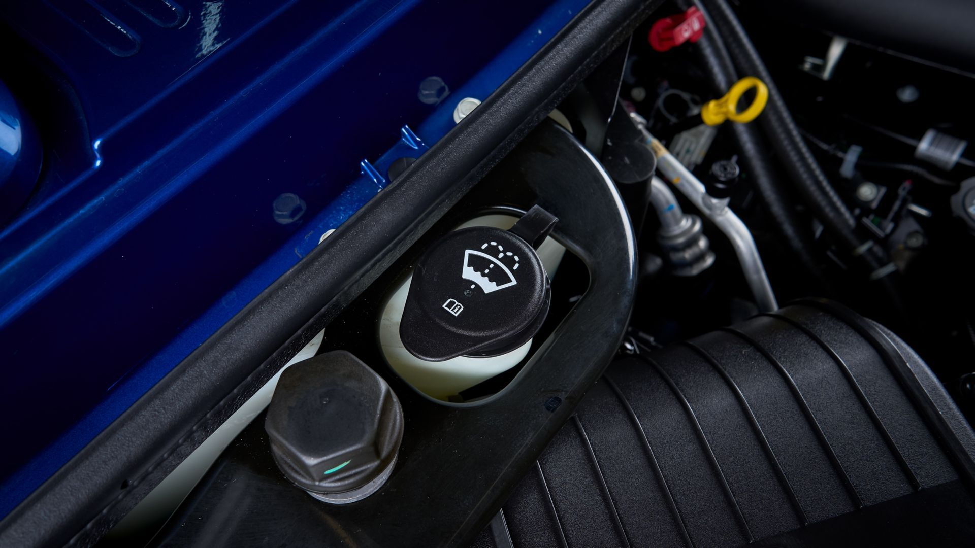 Mechanic in blue coveralls inspecting a car engine with the hood open in a garage