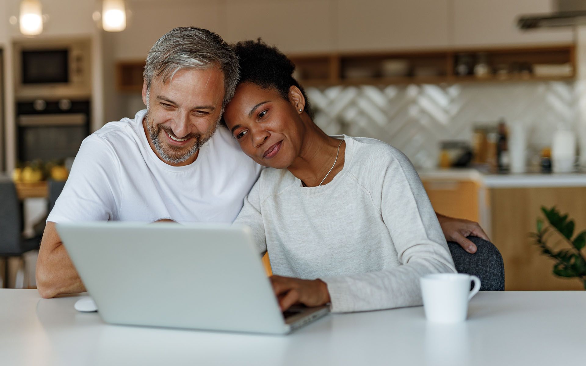 Adults sitting at a kitchen table using a laptop after a D’s Air & Heating installation.