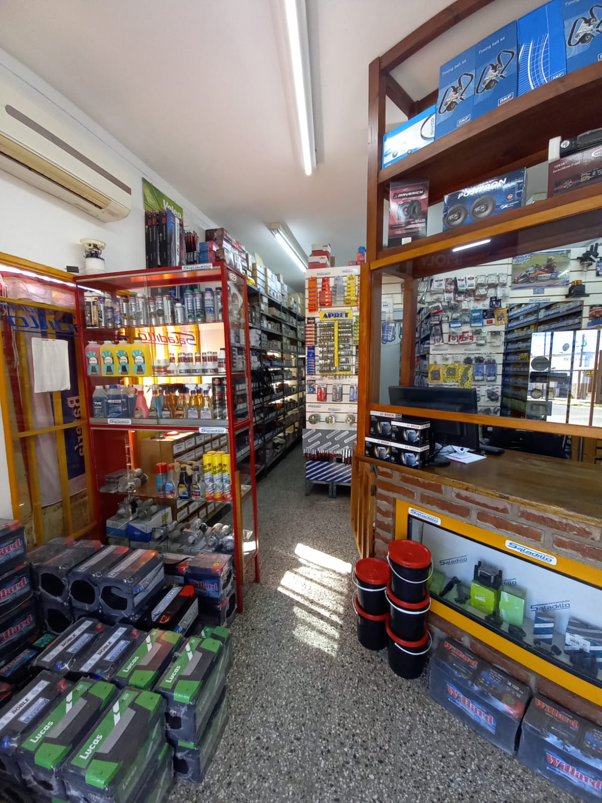 Un estrecho pasillo de una tienda de electrónica, con estantes llenos de herramientas, baterías y artículos embalados