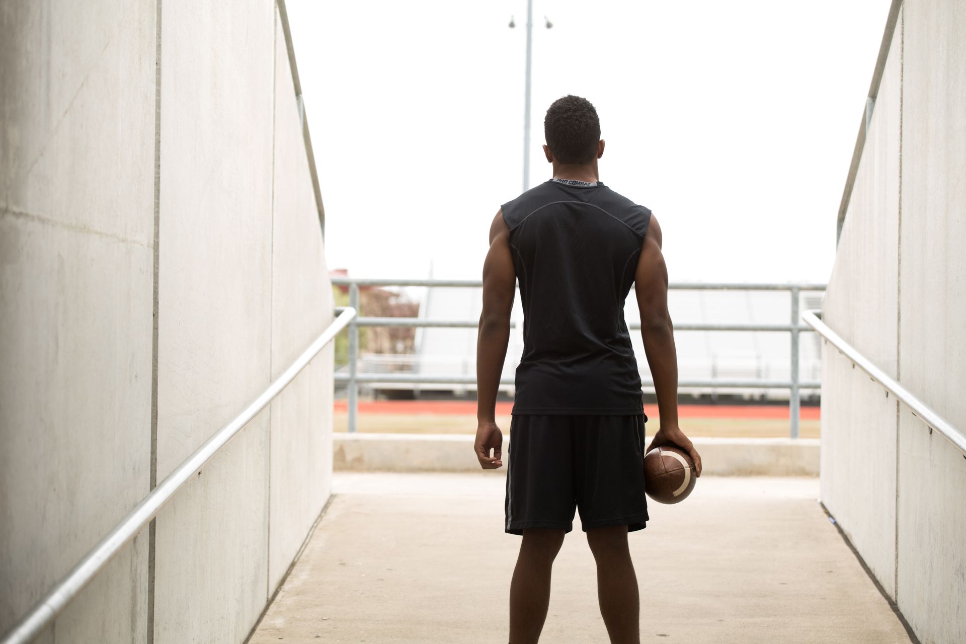 A young athlete holding a football and looking out towards the field in practice clothes
