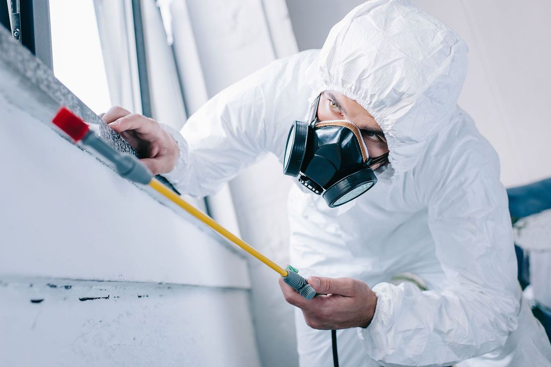 A man in a protective suit and mask is measuring a window.