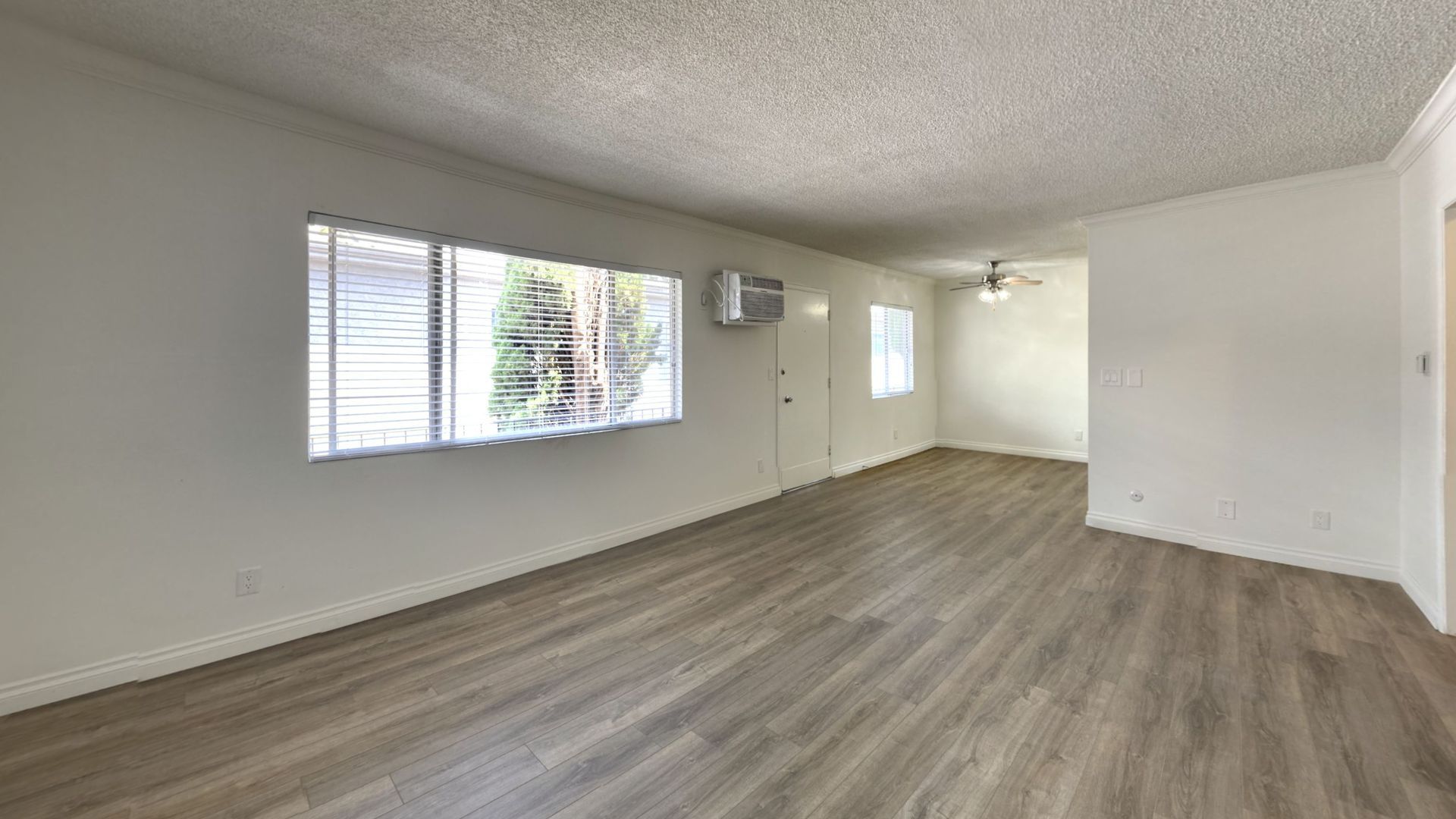 Empty living room with wood-look flooring, white walls, two windows, and an air conditioner.