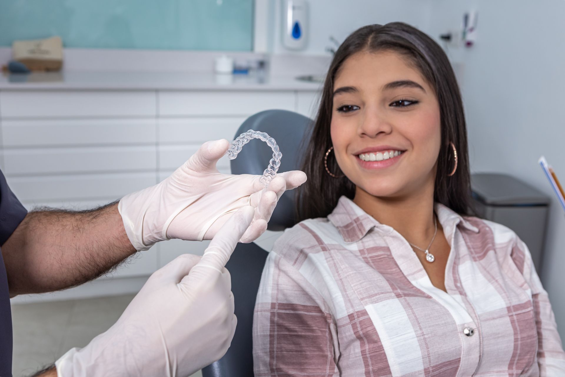 A woman is sitting in a dental chair while a dentist holds a clear brace.