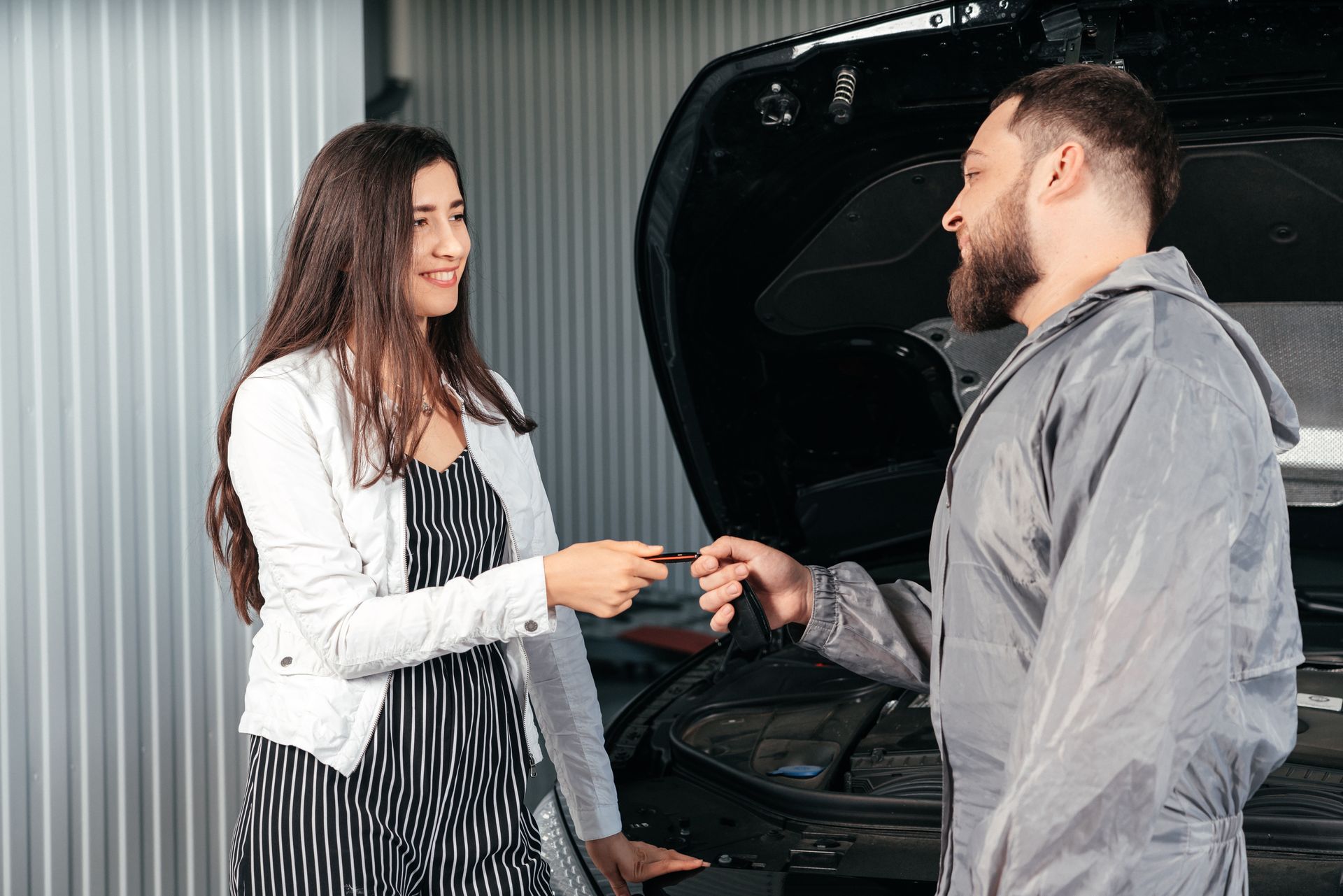 Customer handing car keys to an auto mechanic beside an open vehicle Hood