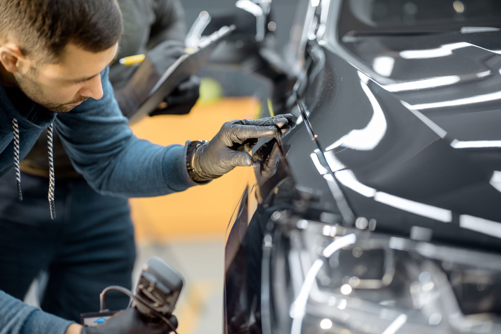 Technicians applying protective film to a car’s exterior in a workshop. Technicians applying protective film to a car’s exterior in a workshop.