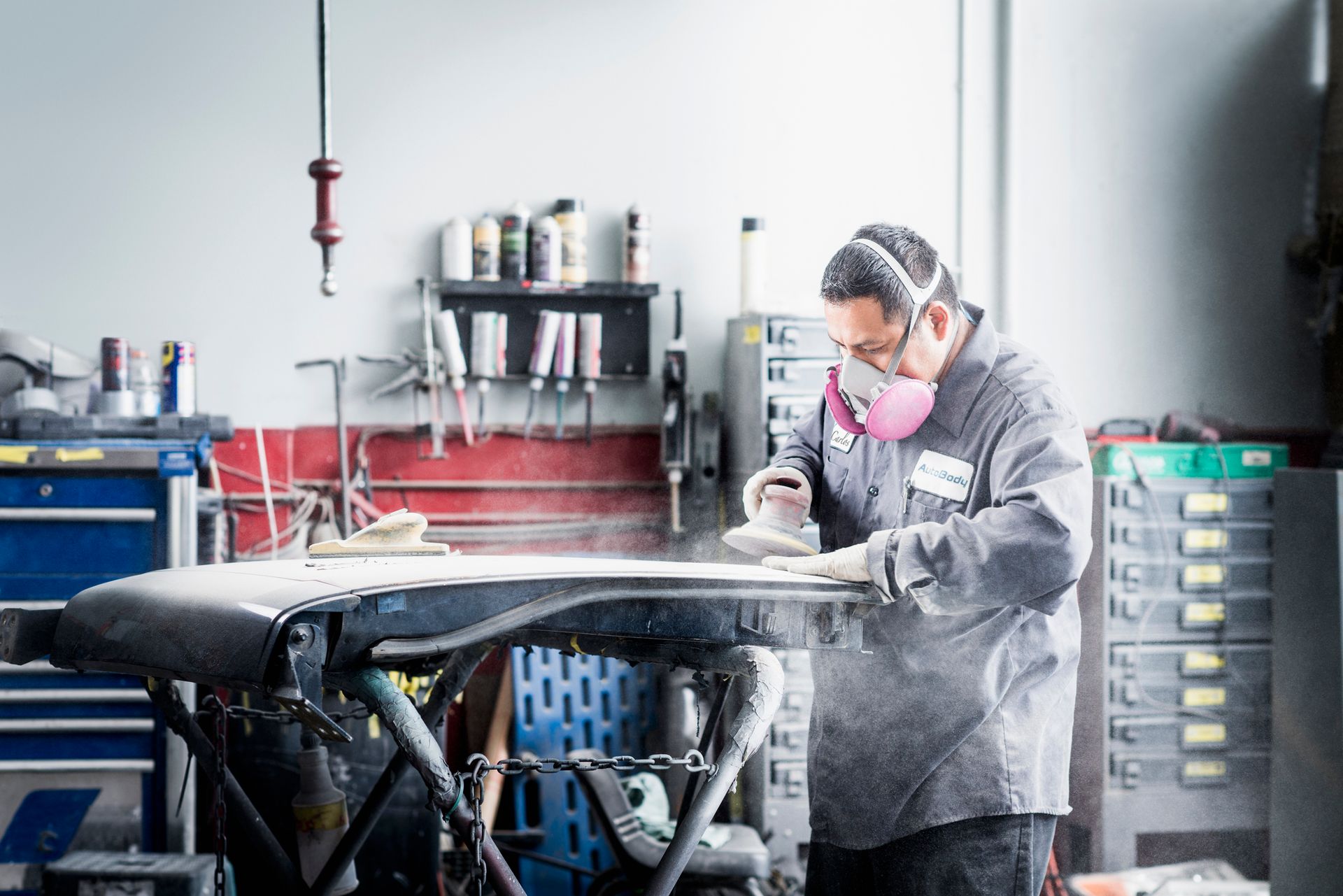 A man at an auto body repair shop works on a car, focused, surrounded by tools and parts. A man at an auto body repair shop works on a car, focused, surrounded by tools and parts.