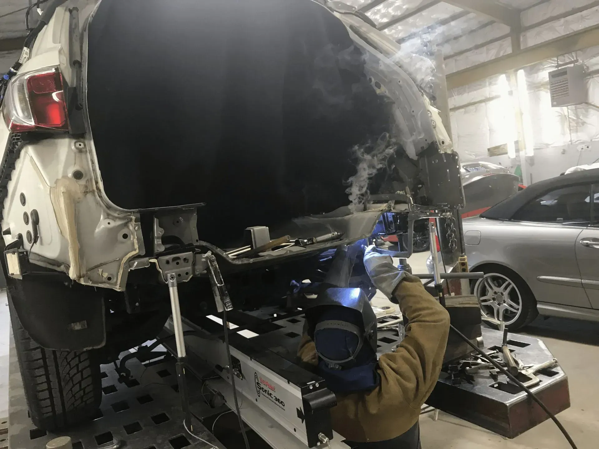 A person welding a car's damaged rear end inside a repair shop.