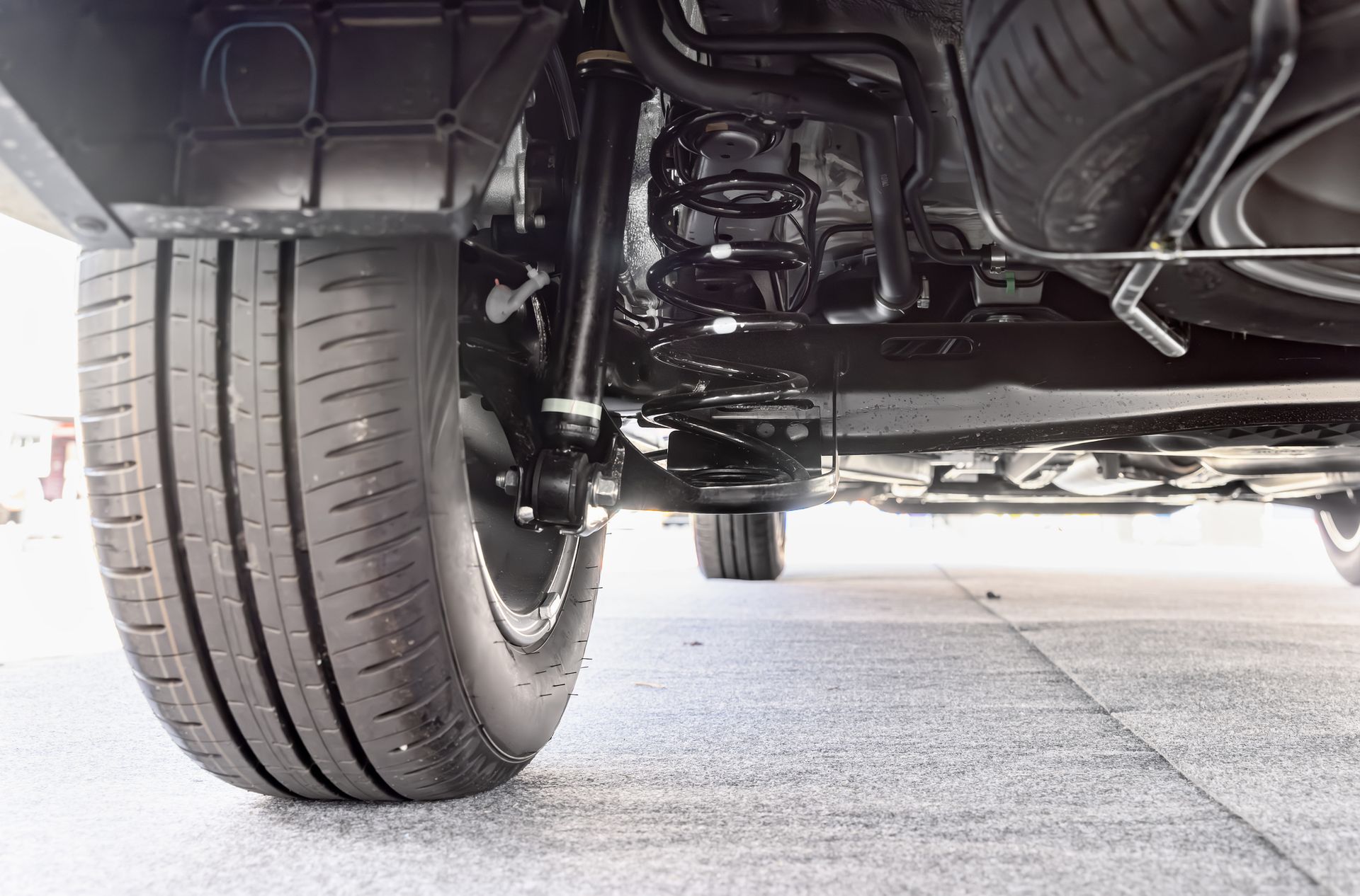 Undercarriage of a car, showing tire, suspension, and spare tire beneath a vehicle on a paved surface.