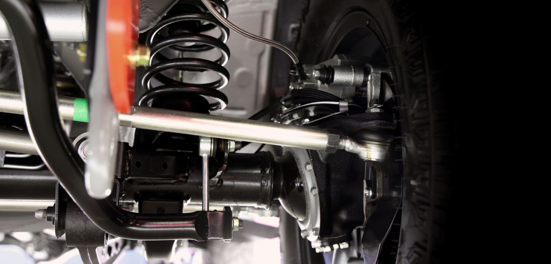 Undercarriage of a vehicle showing suspension components, including a coil spring, control arms, and a steering rod.