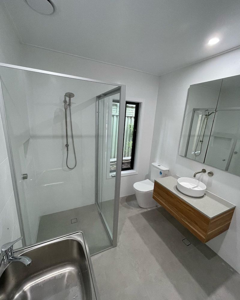 Laundry and bathroom renovation with framed glass shower enclosure, timber grain floating vanity with stone benchtop and round vessel sink, chrome wall-mounted tapware, large format grey porcelain floor tiles, recessed mirror cabinet, and stainless steel laundry tub