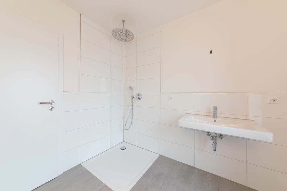 Empty White Tiled Bathroom With Shower, Wall-mounted Sink, and Floor Drain — Firm Built Bathrooms in Illawarra, NSW