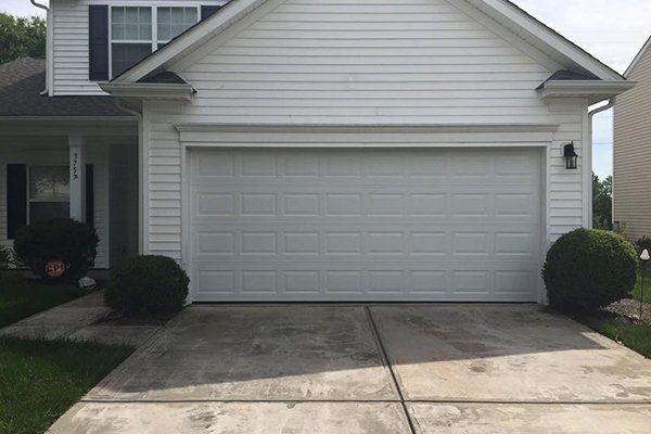Front view of a white two-car garage with a concrete driveway and small bushes