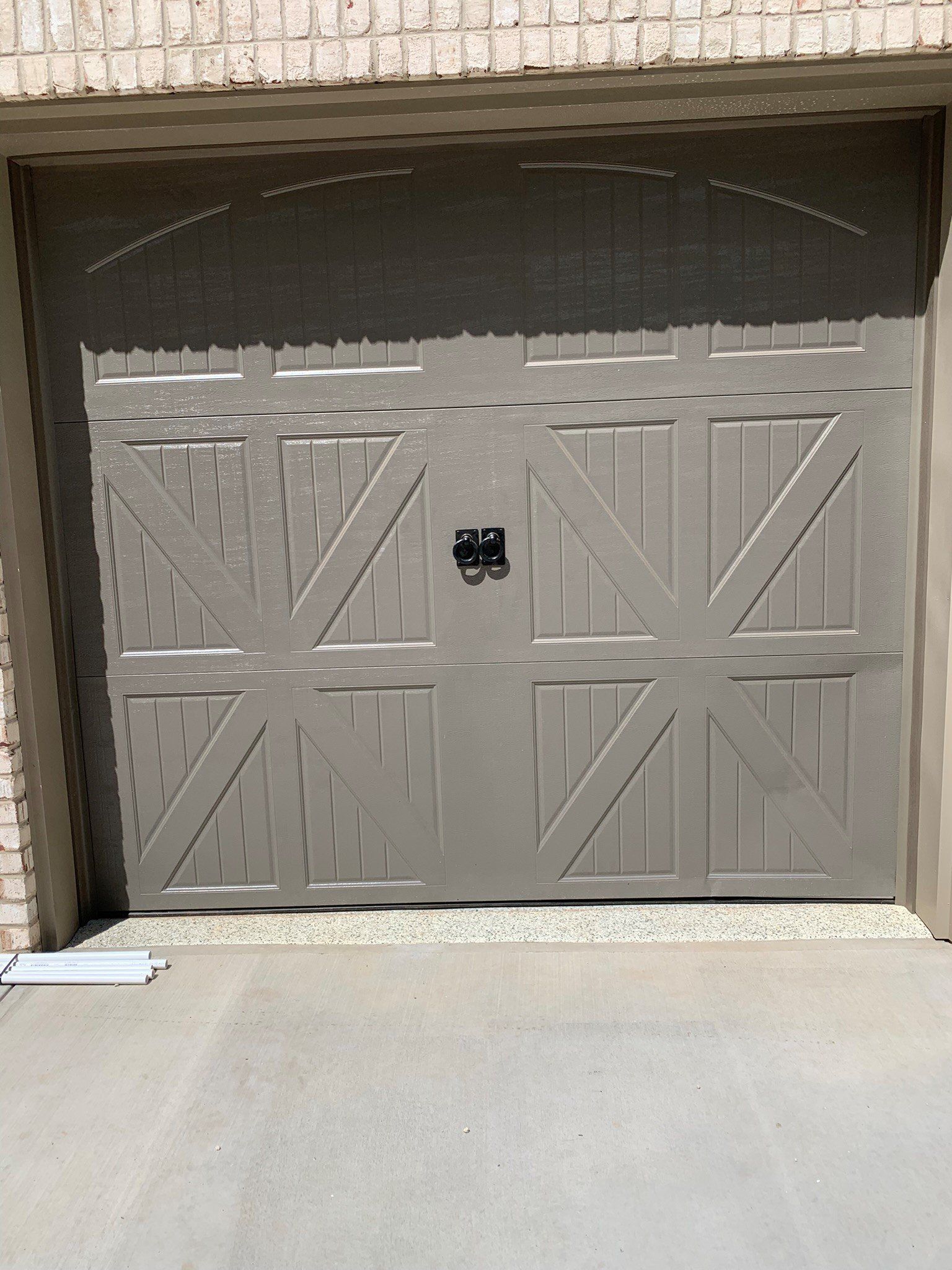 Closed beige garage door with diagonal wood trim and a small black handle, set in a brick opening.