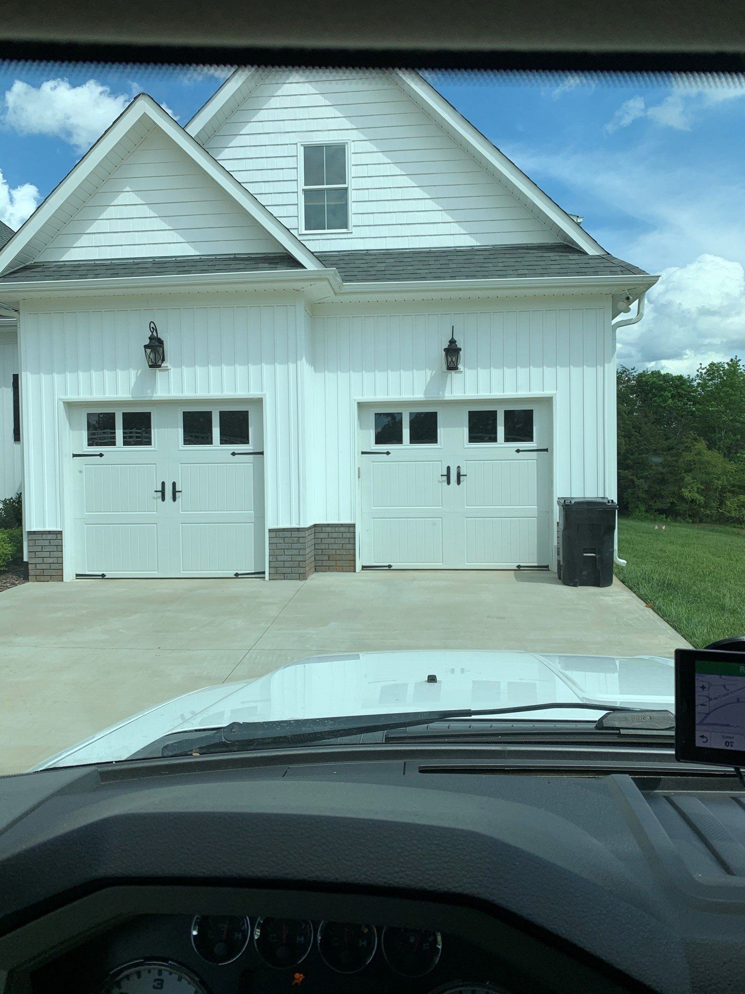 Two white garage doors on a house with a driveway, viewed from inside a car.