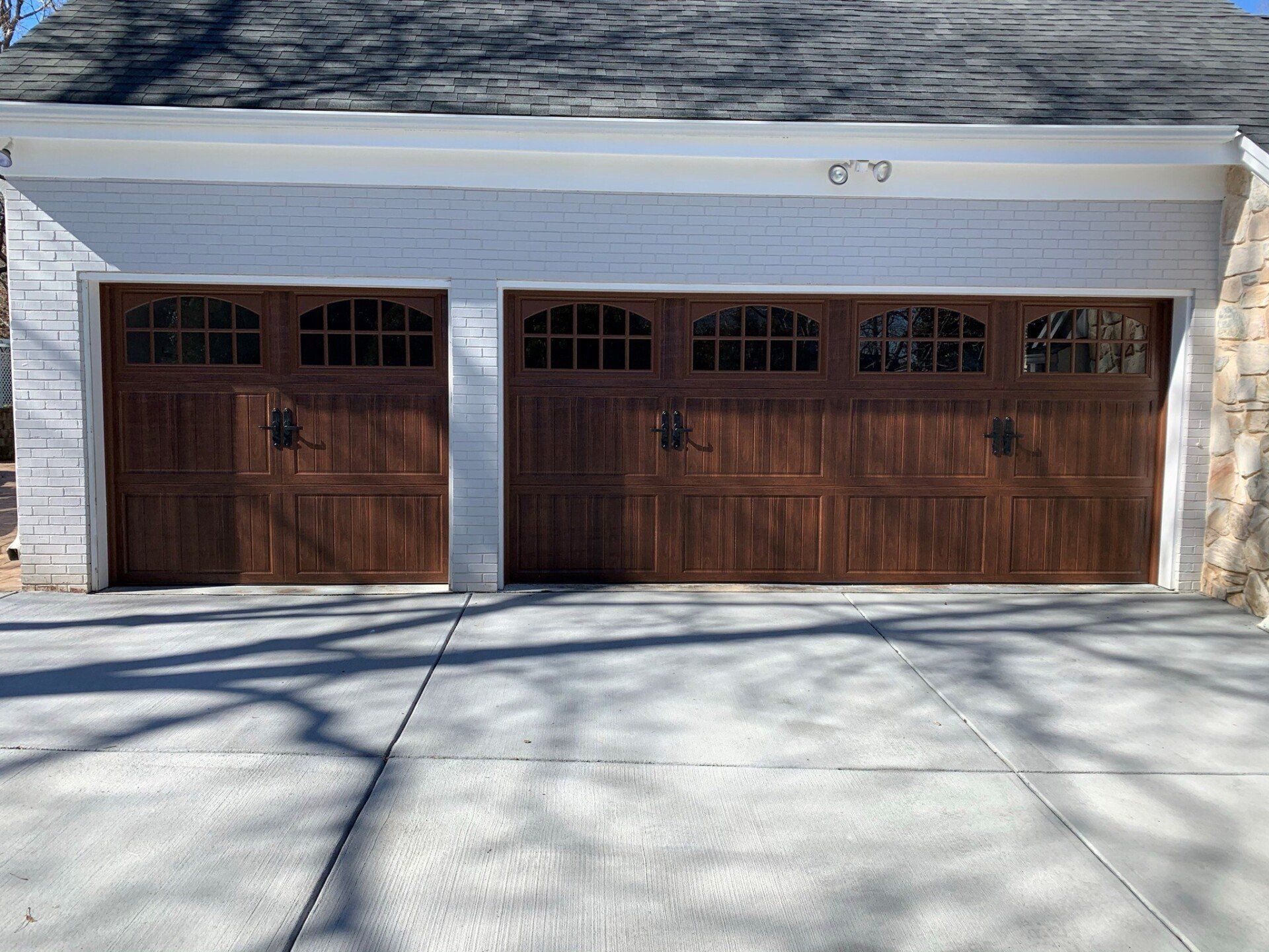 Two wooden garage doors on a white house with a concrete driveway in front