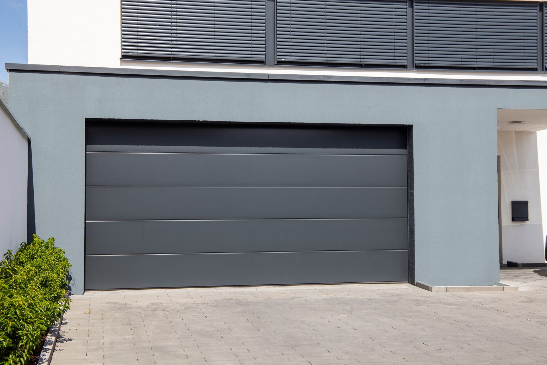 Modern gray sectional garage door on contemporary home exterior with driveway and clean design style.
