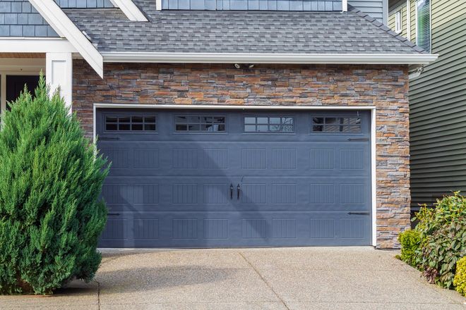 Modern blue garage door with windows on stone exterior of suburban home driveway and curb appeal vie.