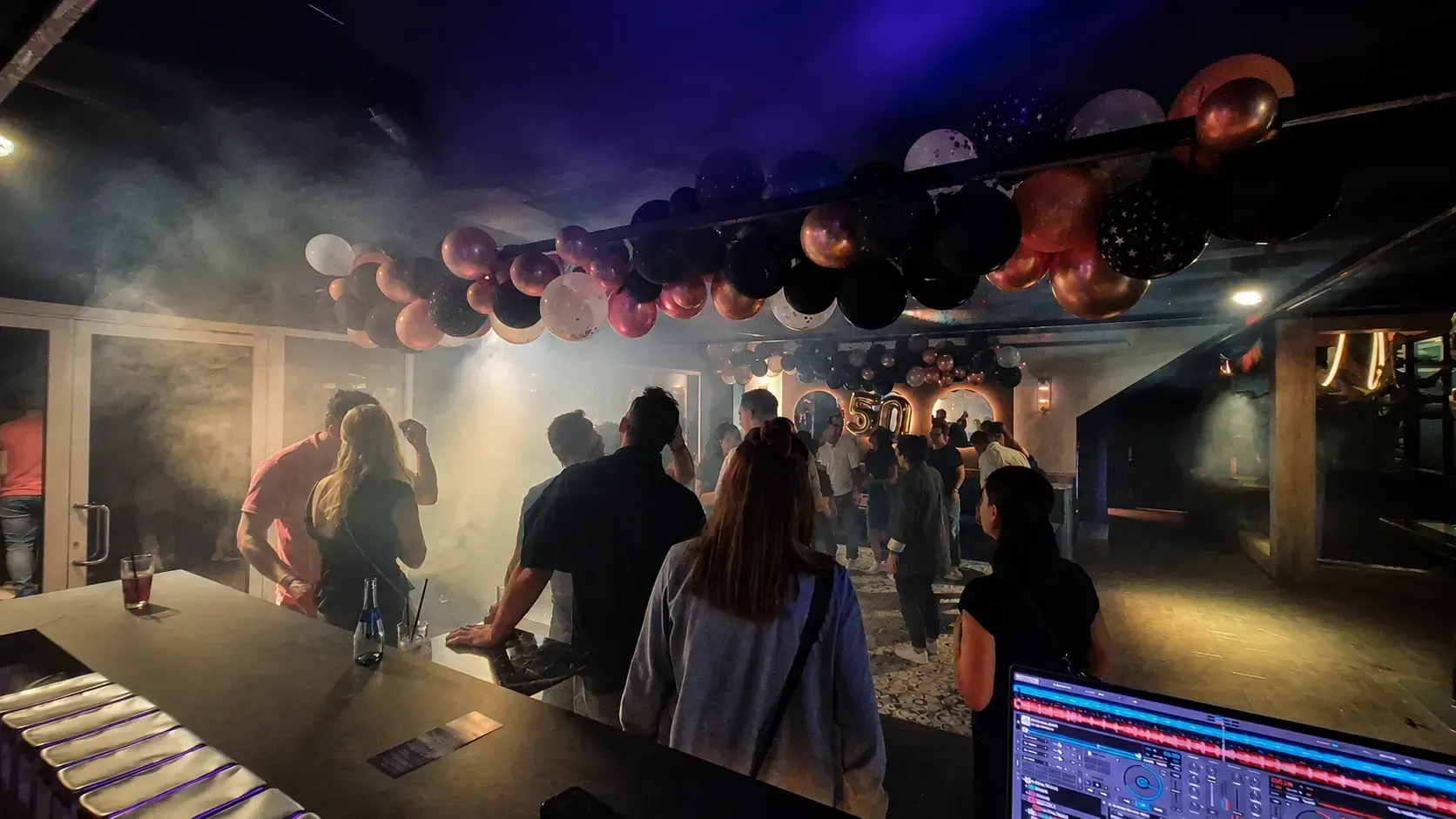 Blick vom DJ-Pult auf eine Party mit Licht und Haze