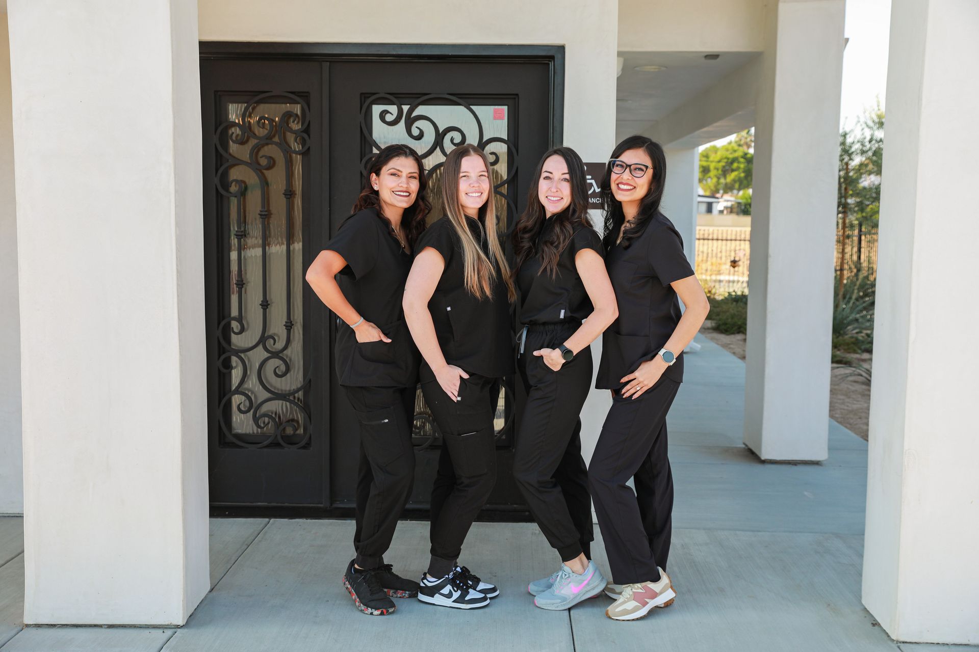 Three smiling women in black shirts standing in front of ornate iron gates