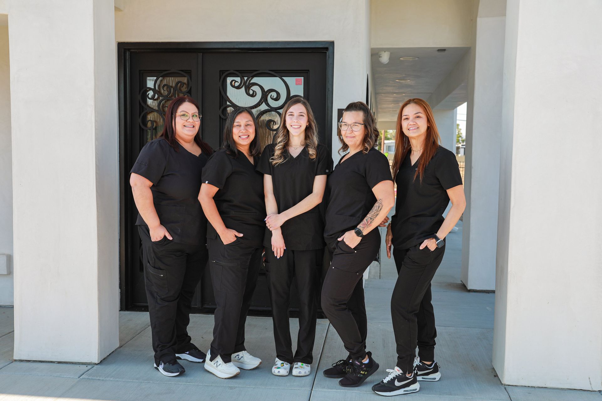 Three smiling women in black shirts standing in front of ornate iron gates