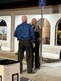 Two people talking on a sidewalk outside a building with arched windows at night